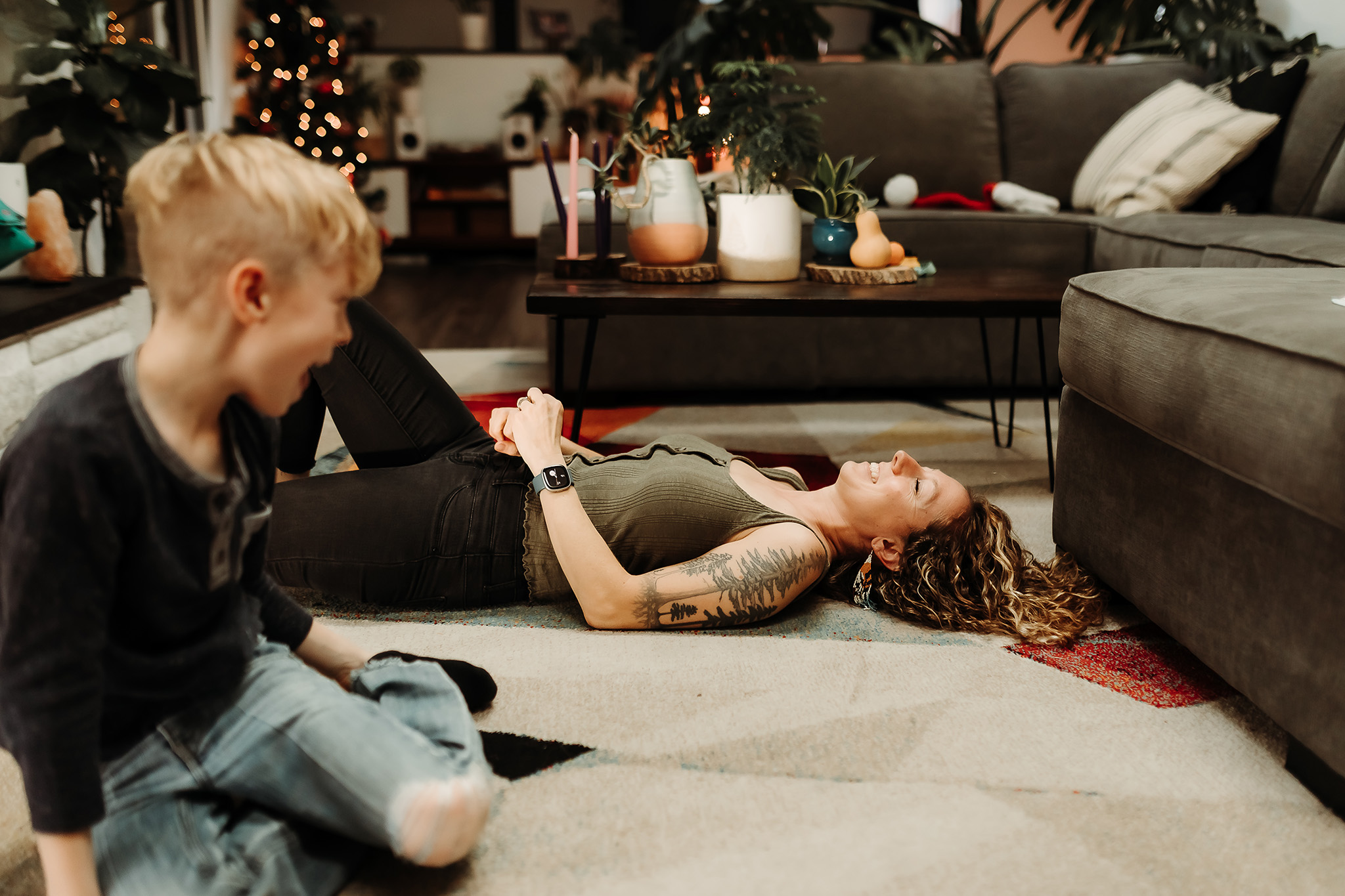 mother lays on the floor of their home in evergreen colorado, smiling and laughing as son looks on