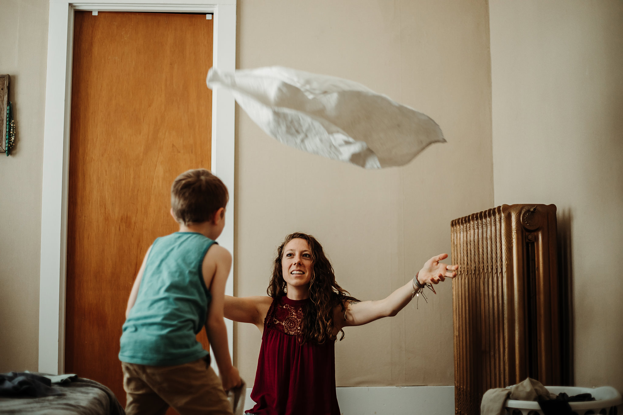 mother tossing laundry to child to catch, playing games as they fold clothes in colorado bedroom