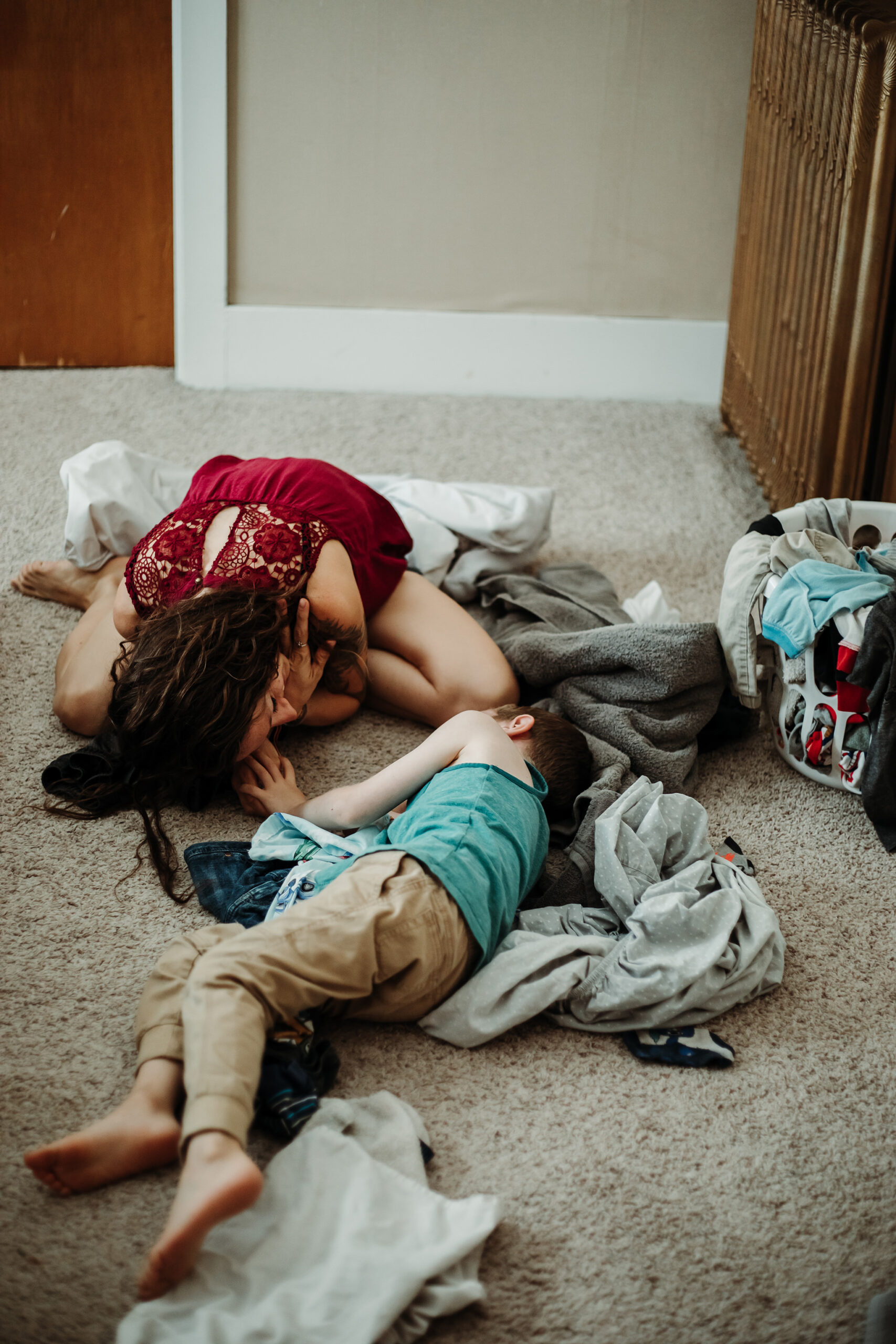 woman and child lying on floor in bedroom with laundry strewn about, documentary style