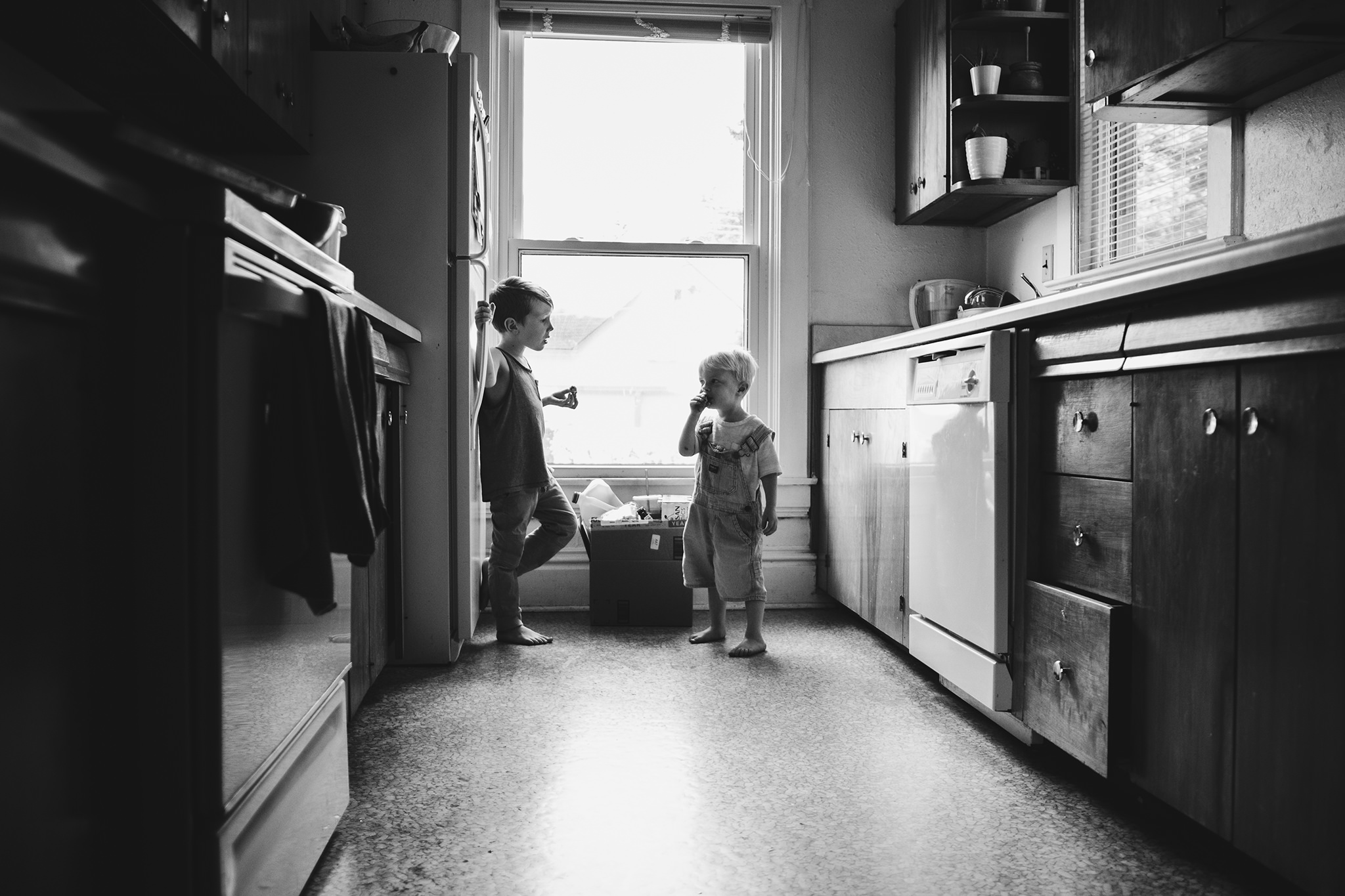 two children in black and white in kitchen eating snacks and talking