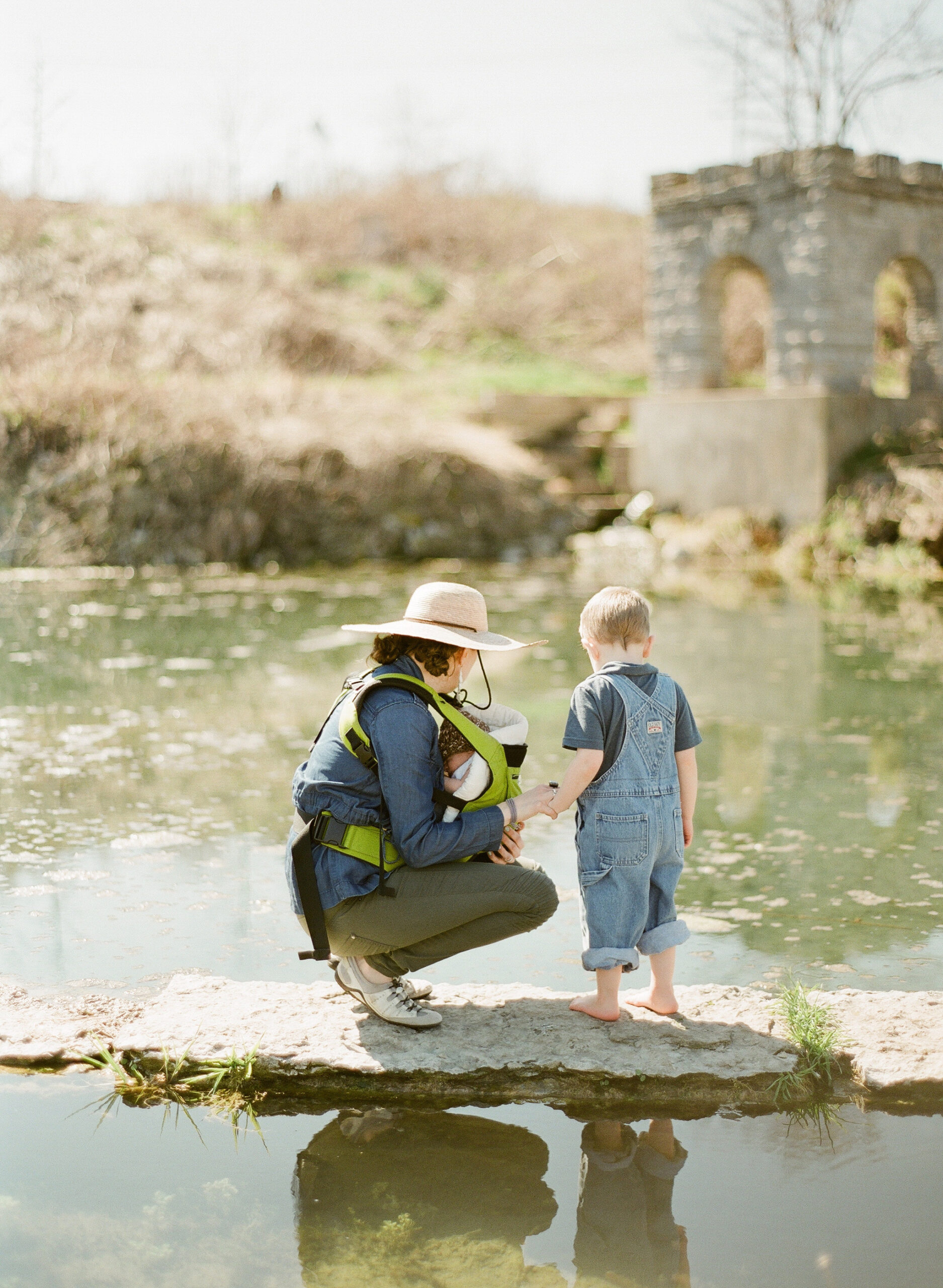 Mother with toddler and baby gaze at the water in park