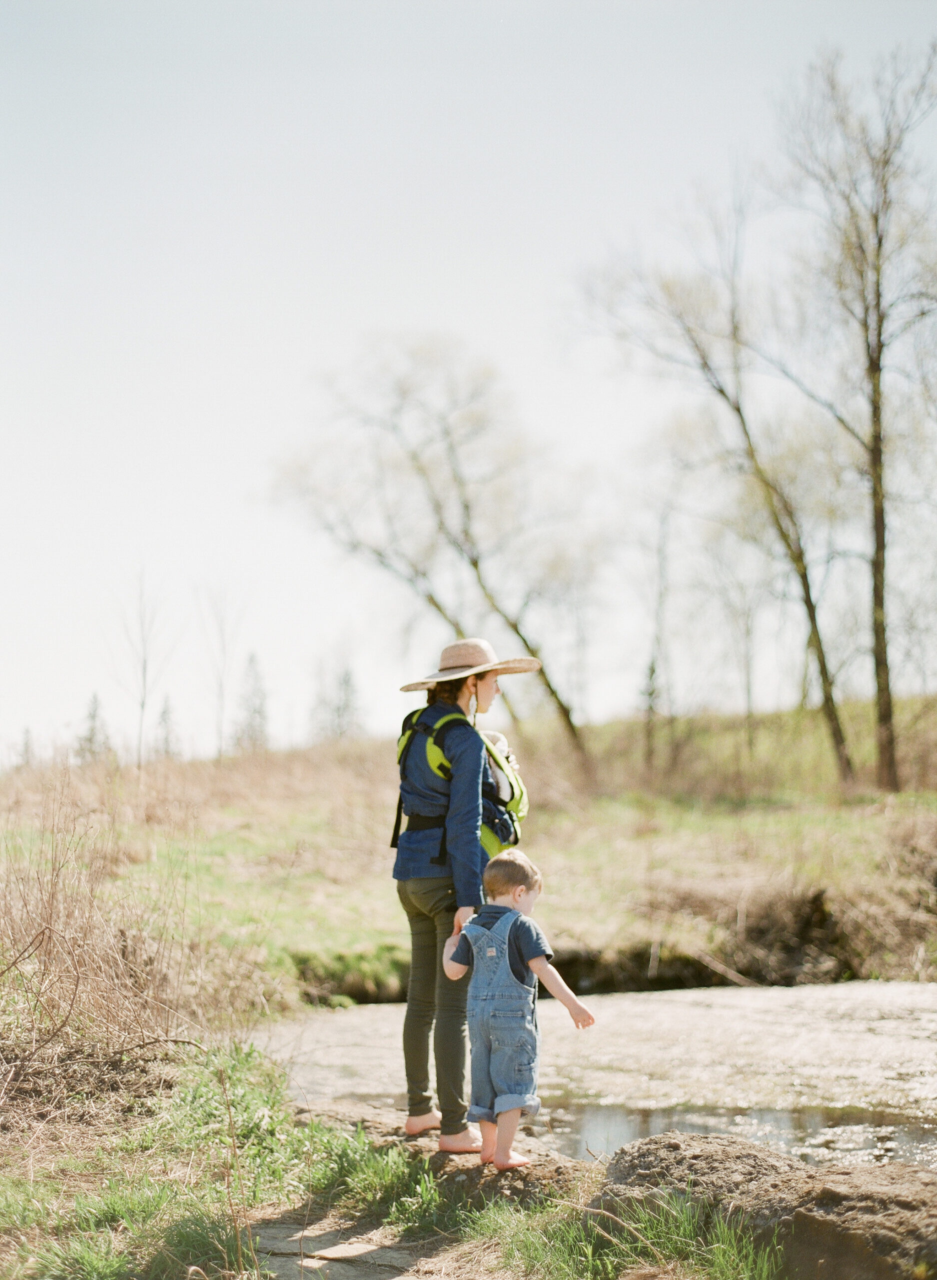 mother and children hold hands while gazing at pond