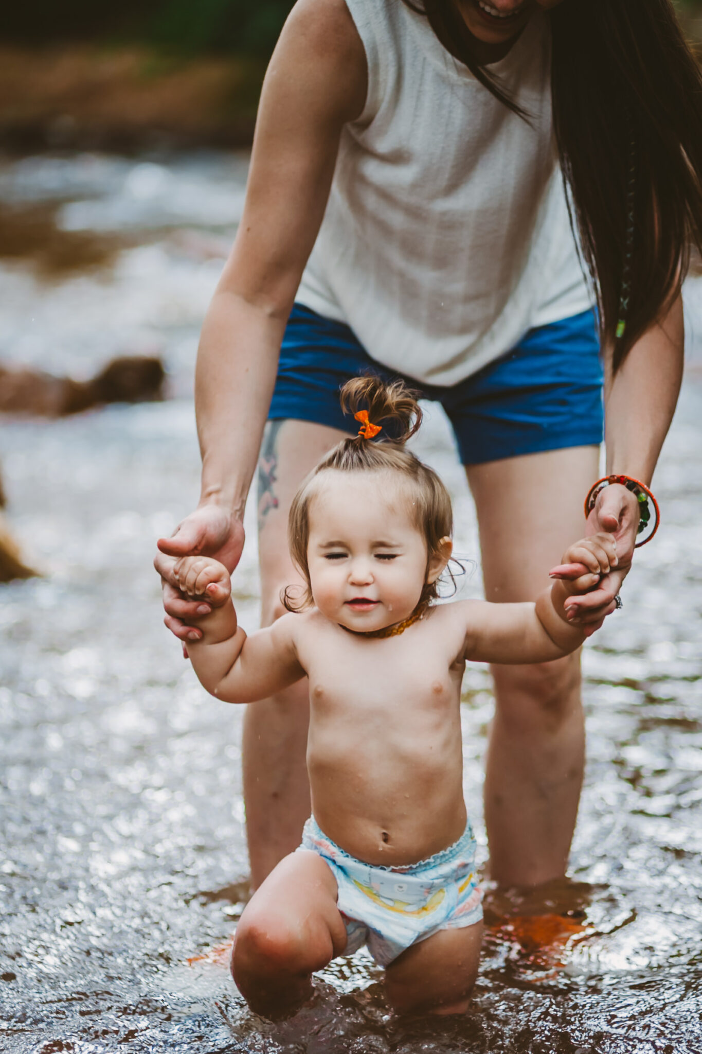 mother holds hands of toddler as she splashes in mountain creek in colorado