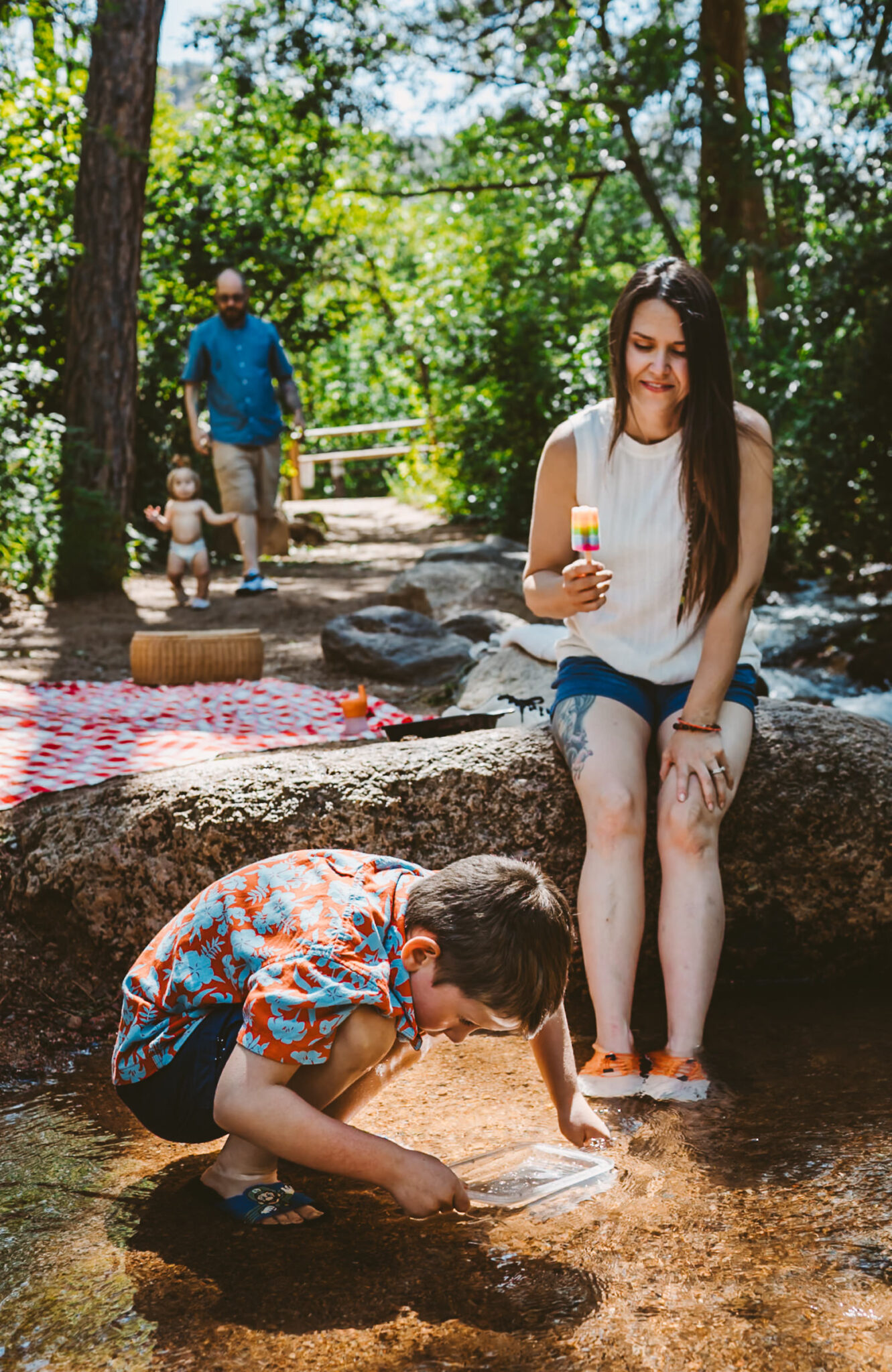 mother eats popscicle as she watches her son pan for gold in colorado mountain creek