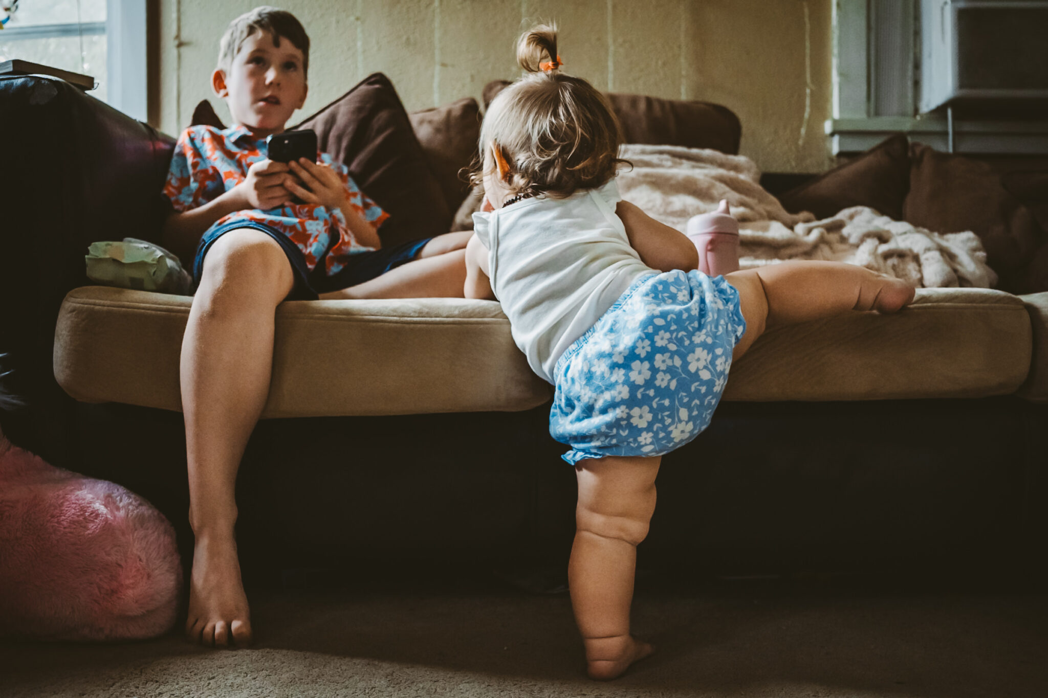 toddler climbs onto couch with brother