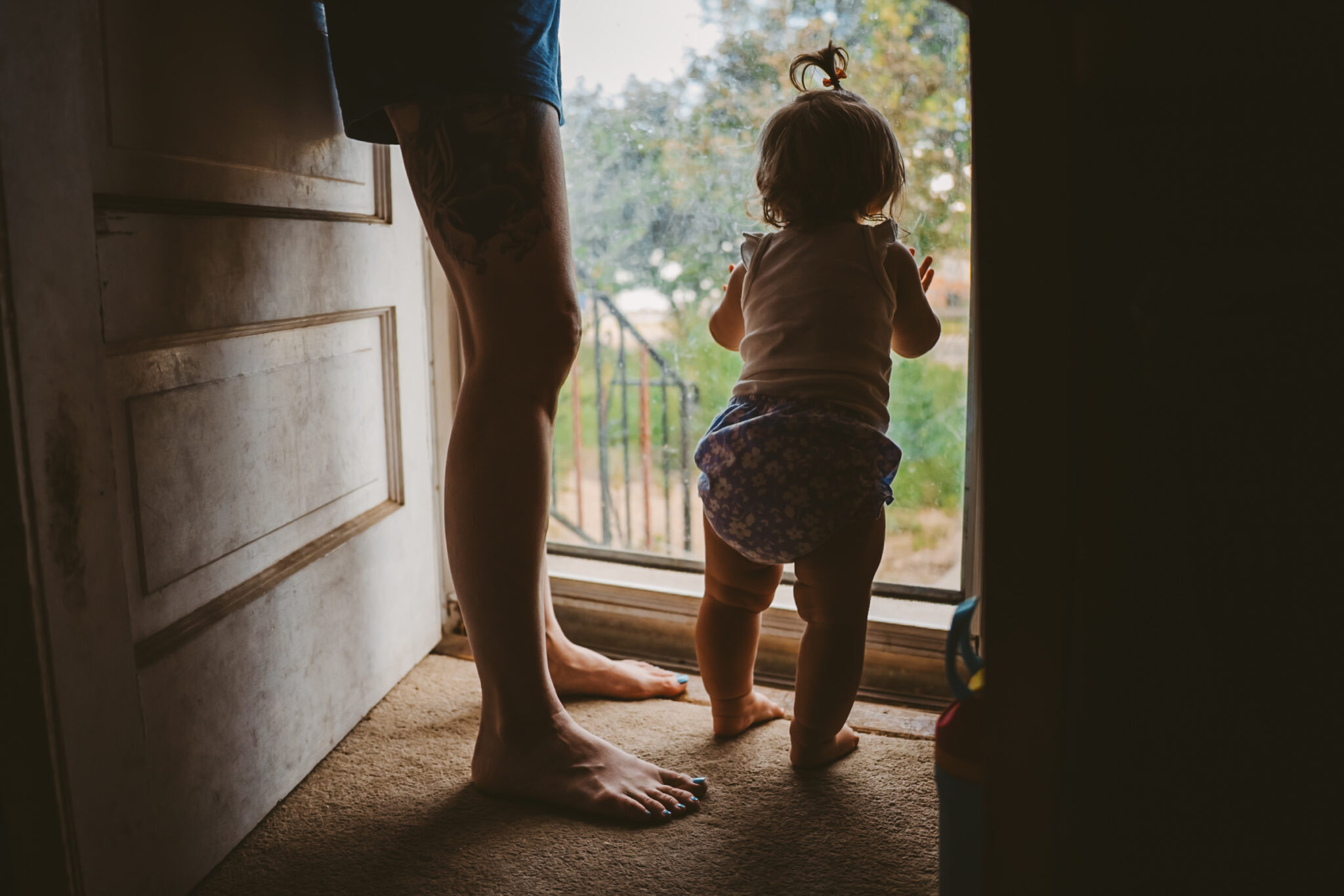toddler looks out the front door silhouetted with mother's legs